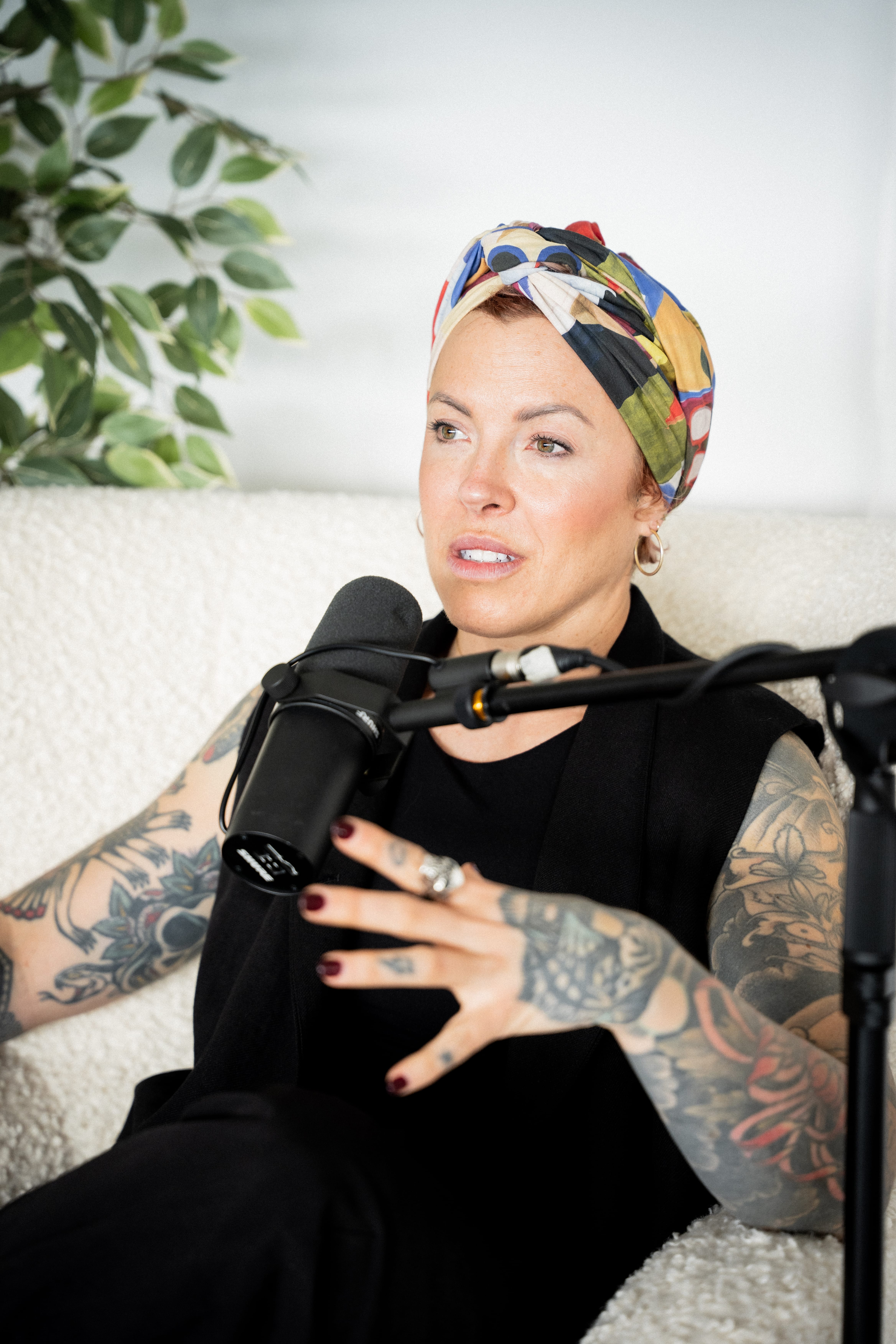 María Lasa hablando frente a un micrófono, con un pañuelo estampado en la cabeza y los brazos tatuados a la vista, sentada en un sofá claro
